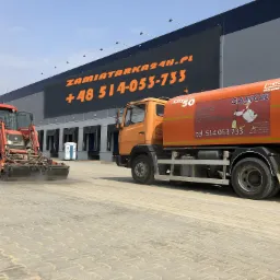 Pomarańczowa zamiatarka uliczna marki Bucher Schorling z logo 'Gąsior' i numerem telefonu, obok czerwony traktor z zamiatarką, na tle magazynu z dużym napisem 'Zamiatarka24h.pl'.