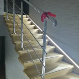 Jasne, drewniane schody z nowoczesną, metalową barierką w Białobrzegach, ozdobioną czerwoną wstążką, oświetlone delikatnym światłem LED.