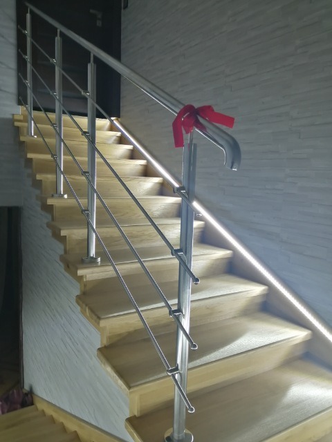 Jasne, drewniane schody z nowoczesną, metalową barierką w Białobrzegach, ozdobioną czerwoną wstążką, oświetlone delikatnym światłem LED.