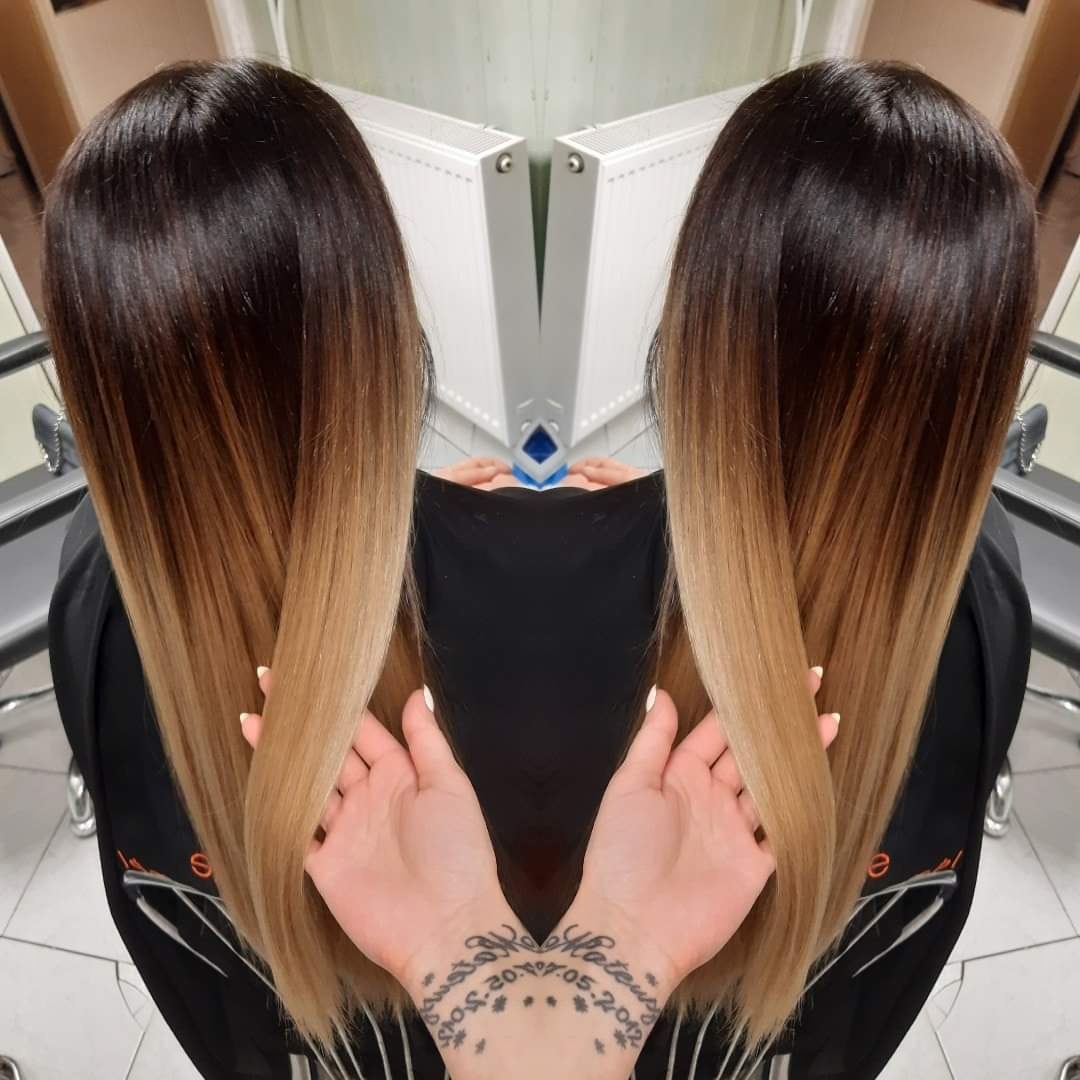 Włosy ombre z ciemnego brązu przechodzące w jasny blond, uchwycone z tyłu, z widocznymi dłońmi modelki z tatuażem na nadgarstku.
