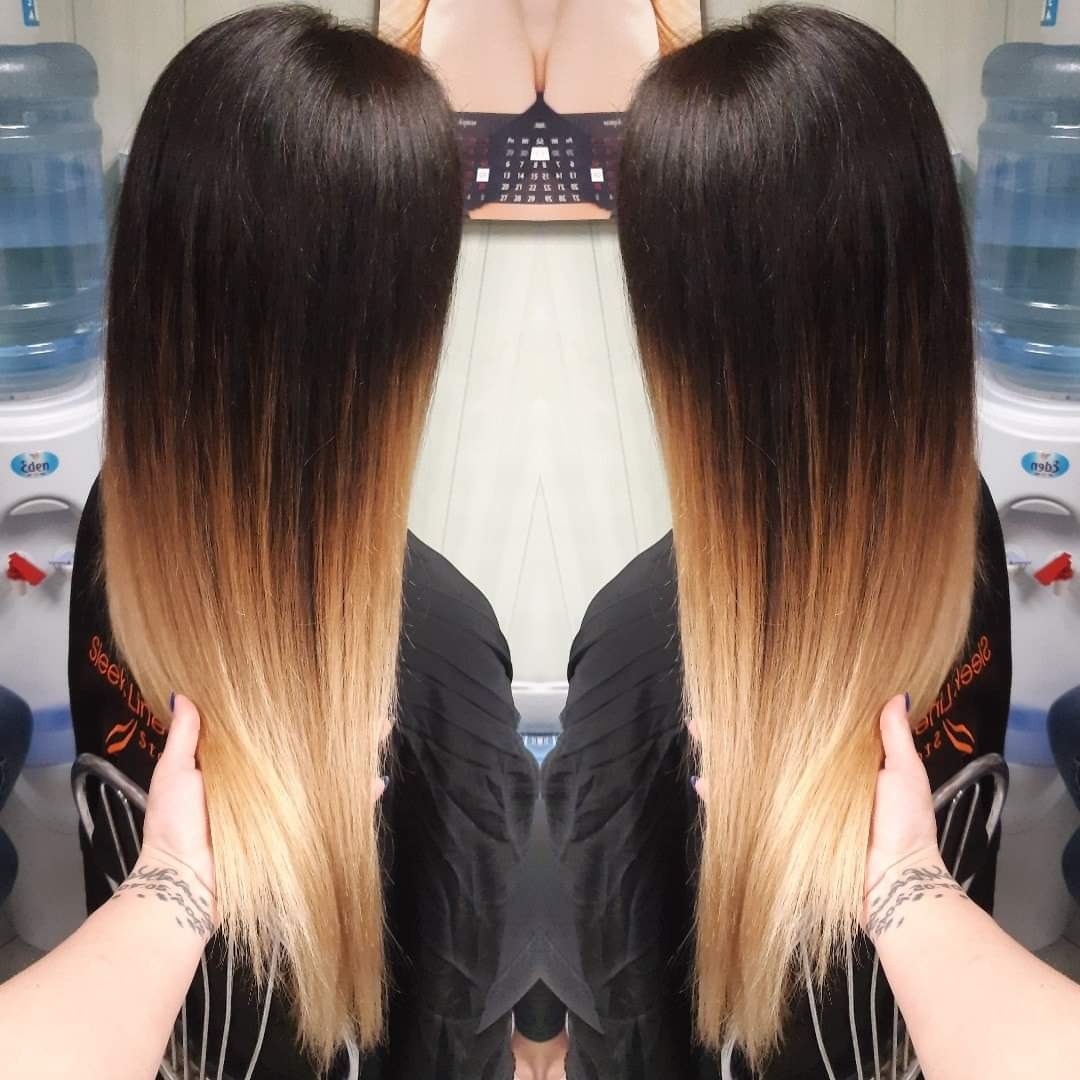 Włosy ombre, od ciemnego brązu u nasady do jasnego blondu na końcach, widoczne z tyłu, trzymane w dłoni z tatuażem na nadgarstku, na tle ściany i dystrybutora wody.