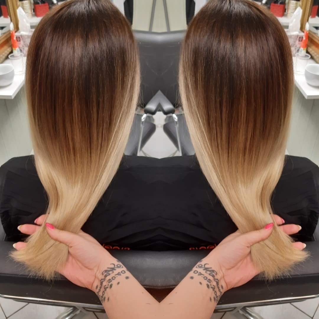 Włosy ombre, brąz u nasady przechodzący w blond na końcach, prezentowane z tyłu w salonie w Wołominie, dłonie z tatuażami podtrzymują pasma.