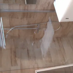 Kabina prysznicowa z brązowymi płytkami imitującymi drewno, zamontowana bateria natryskowa z deszczownicą i dyszami, widoczne mocowania szklanej ścianki.