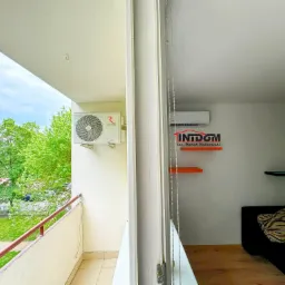 Klimatyzator Rotenso na balkonie mieszkania z widokiem na zieleń, drugi klimatyzator widoczny w pokoju za przeszkleniem.