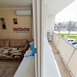 INTDOM MAREK KALINOWSKI - Widok z balkonu na dwa zamontowane klimatyzatory na zewnątrz. W tle budynki mieszkalne i zieleń. Wnętrze mieszkania z klimatyzatorem widoczne po lewej stronie.