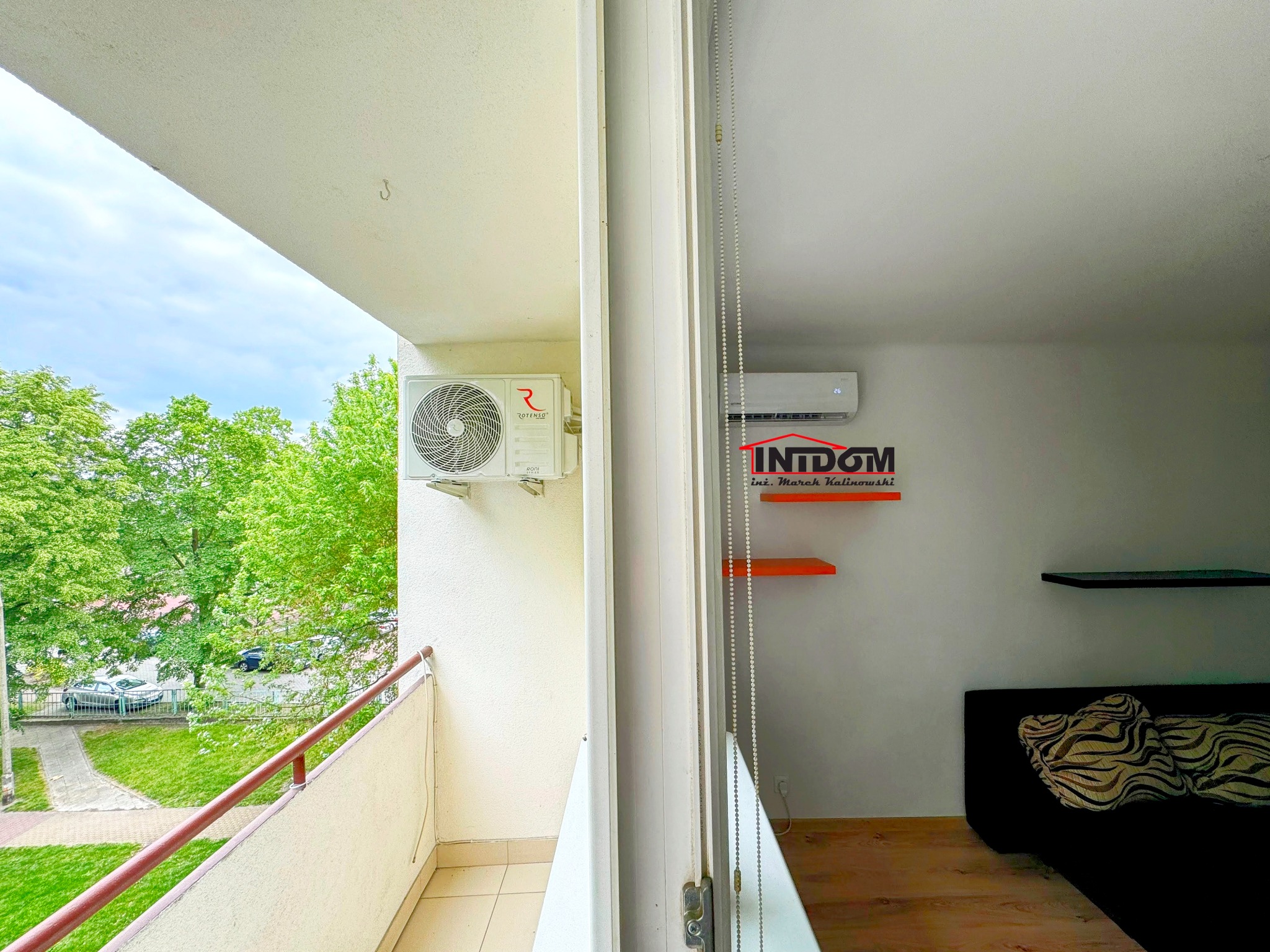 Klimatyzator Rotenso na balkonie mieszkania z widokiem na zieleń, drugi klimatyzator widoczny w pokoju za przeszkleniem.