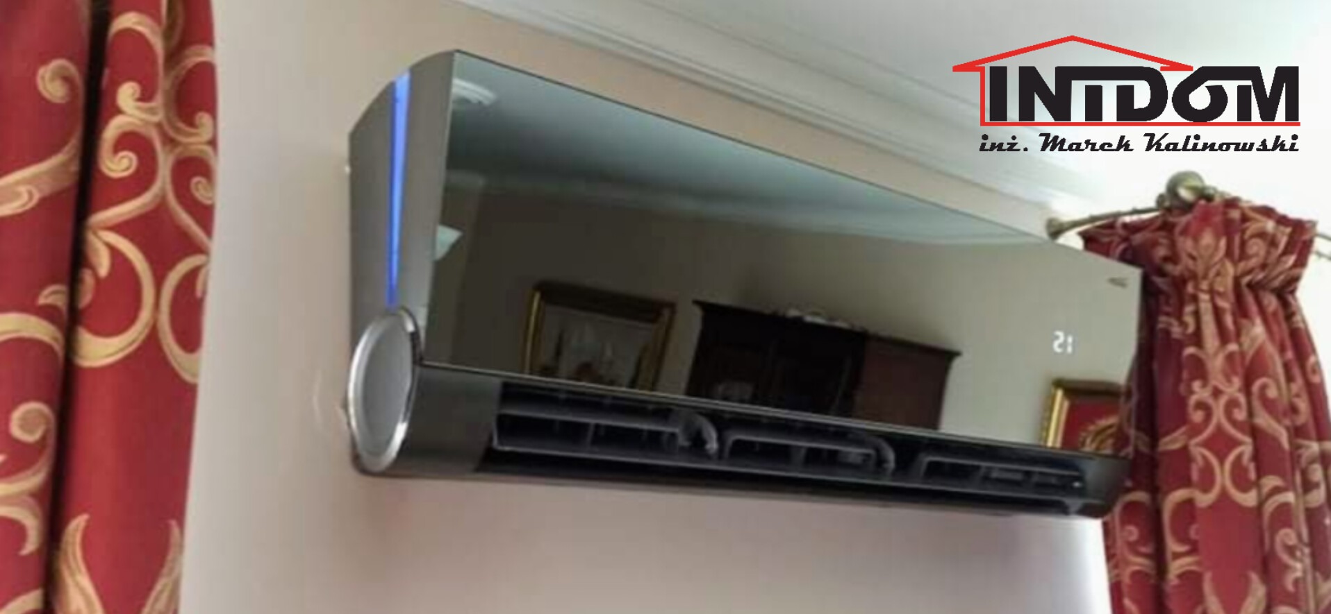 Nowoczesny klimatyzator ścienny z lustrzanym panelem, zamontowany w eleganckim wnętrzu. Widoczne detale wykończenia i logo firmy na tle dekoracyjnych zasłon.