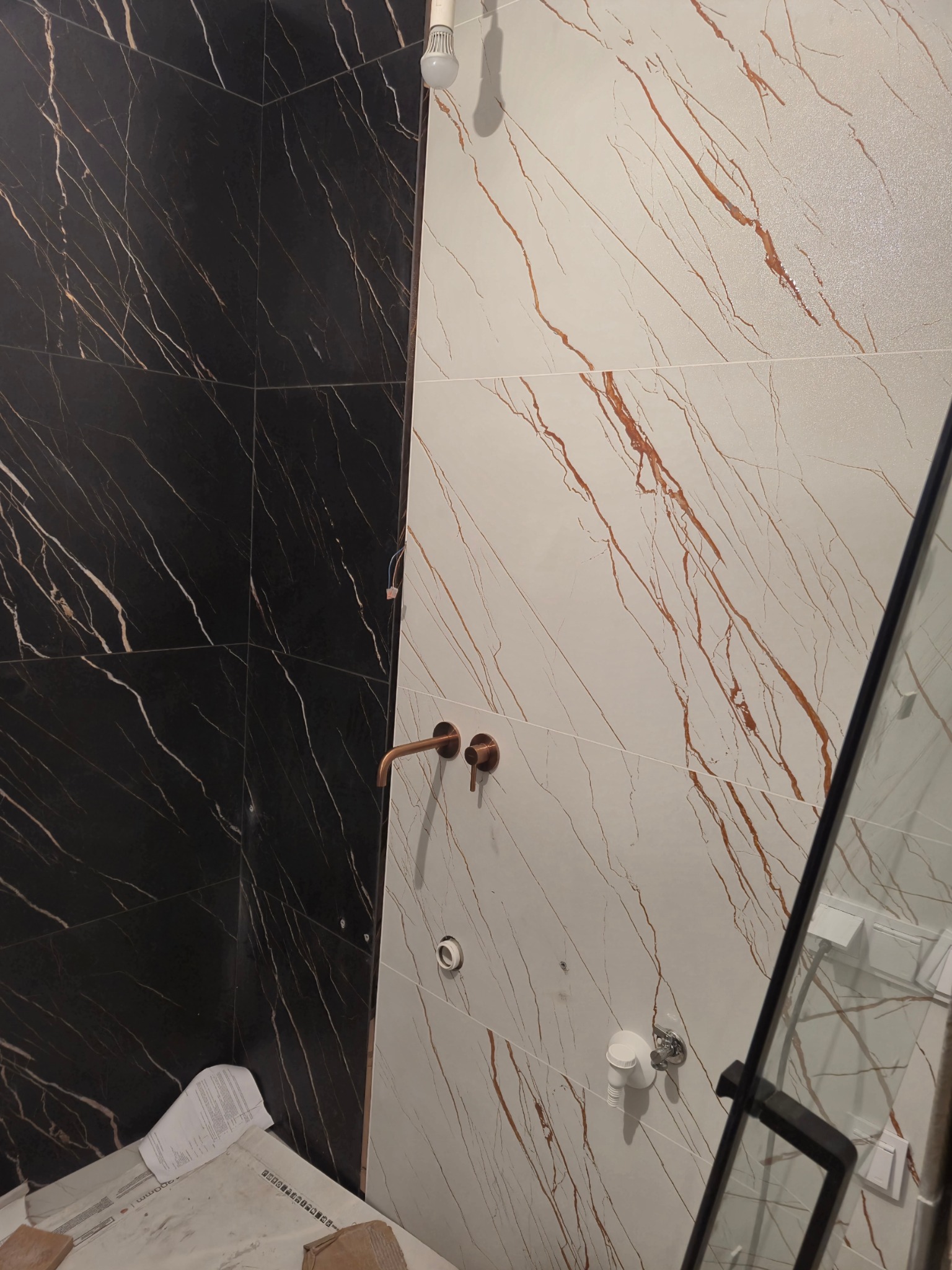 Montaż baterii w łazience z czarno-białymi płytkami imitującymi marmur, widoczne przewody i niedokończone prace.