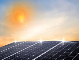 Panele słoneczne na tle błękitnego nieba z pomarańczową poświatą słońca, odbijające światło.