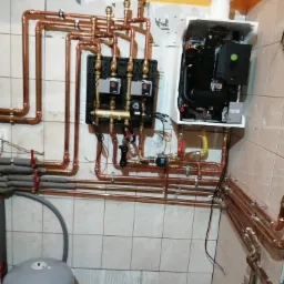 Świeżo zamontowany piec gazowy z miedzianą instalacją w Gnieźnie, widoczne liczne rury i zawory, na ścianie płytki ceramiczne.