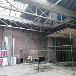 Wnętrze remontowanego budynku z odsłoniętą cegłą, widoczne rusztowania, materiały izolacyjne Rockwool, blachy i elementy konstrukcji dachu z oknami.