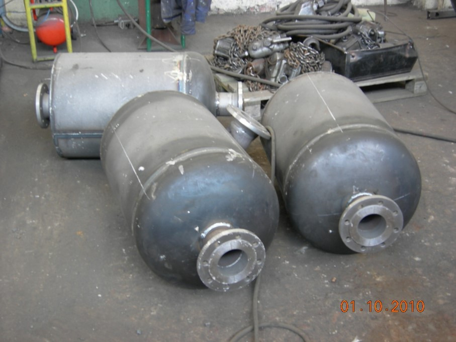 Trzy stalowe, cylindryczne zbiorniki z kołnierzami, leżące na szarej betonowej podłodze warsztatu, z widocznymi śladami spawania i elementami wyposażenia w tle.