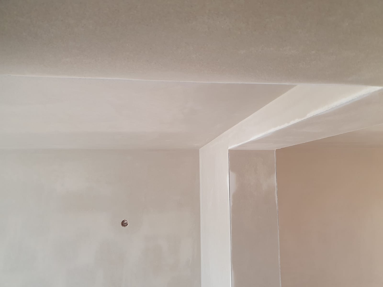 Świeżo położone, jasne tynki maszynowe na ścianach i suficie wewnątrz budynku, widoczny otwór na gniazdko elektryczne i fragment ościeżnicy.