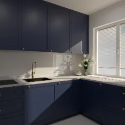Nowoczesna kuchnia z granatowymi szafkami, złotą armaturą i białym blatem, doświetlona naturalnym światłem z okna z żaluzjami.