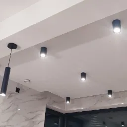 Nowoczesne oświetlenie sufitowe z czarnymi, cylindrycznymi lampami wiszącymi i punktowymi w białym wnętrzu z marmurowym wykończeniem ścian.