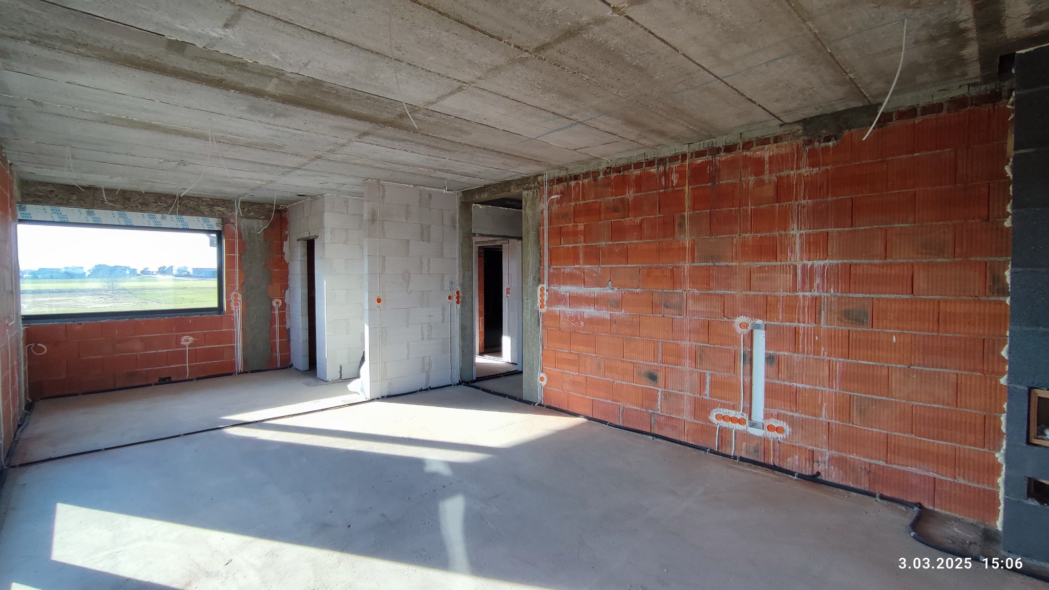 Surowy stan wnętrza budynku w trakcie instalacji elektrycznej: widoczne przewody w ścianach z cegieł, puszki elektryczne, betonowy sufit i wylewka podłogowa.