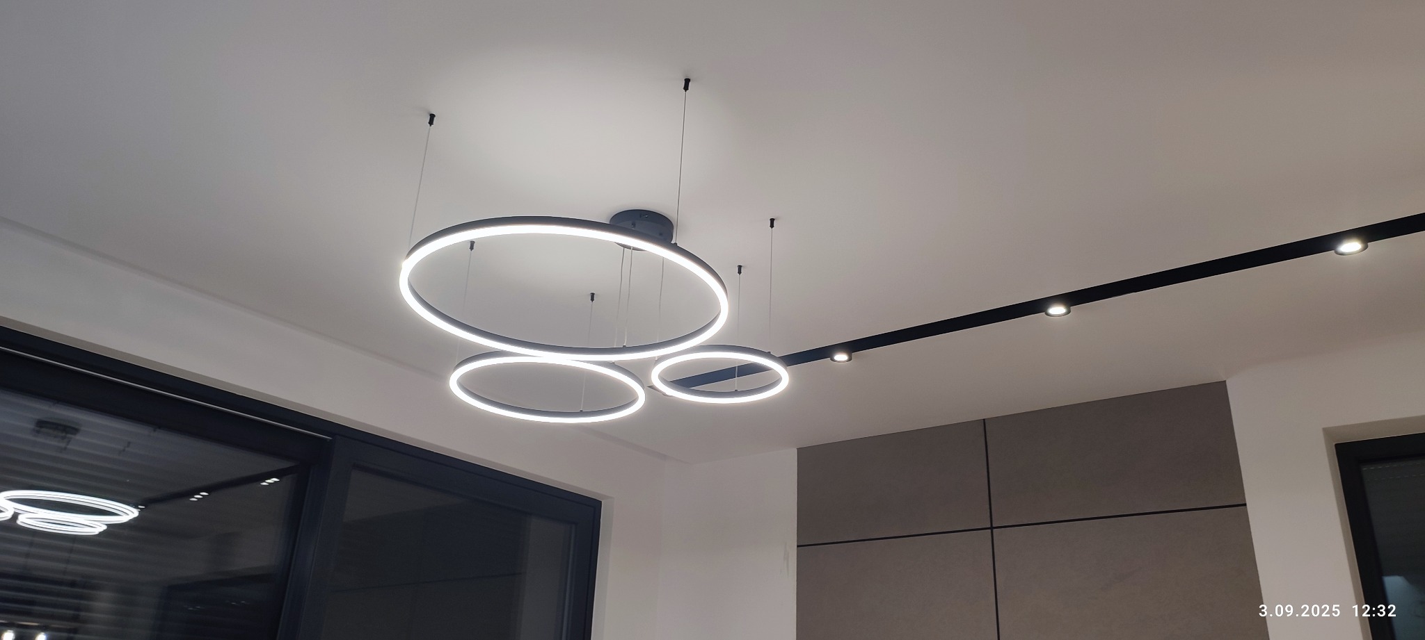 Nowoczesne oświetlenie sufitowe: trzy okrągłe lampy LED zawieszone obok szyny z reflektorami punktowymi, czarne ramy, jasne, białe światło, minimalistyczny design.