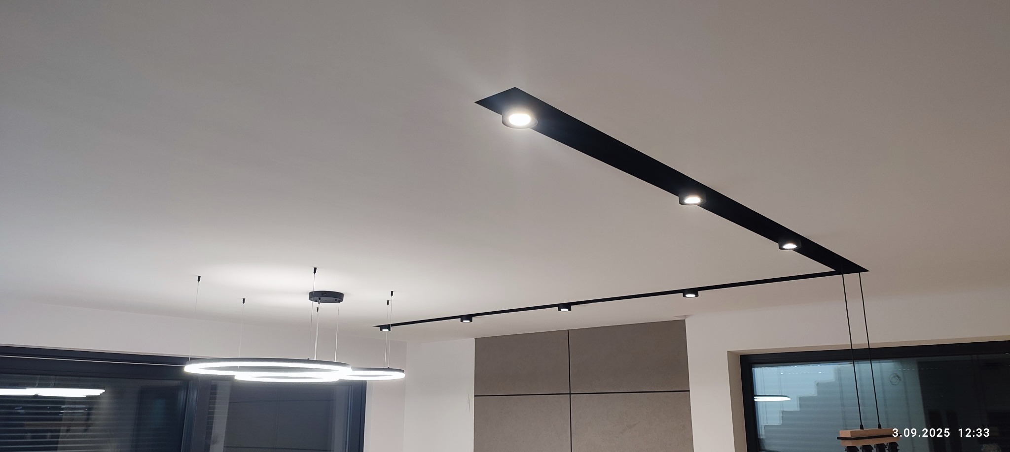 Nowoczesne oświetlenie sufitowe: czarne szyny z reflektorami i okrągłe lampy wiszące w minimalistycznym wnętrzu. Górny kadr, widok na sufit i część wyposażenia.