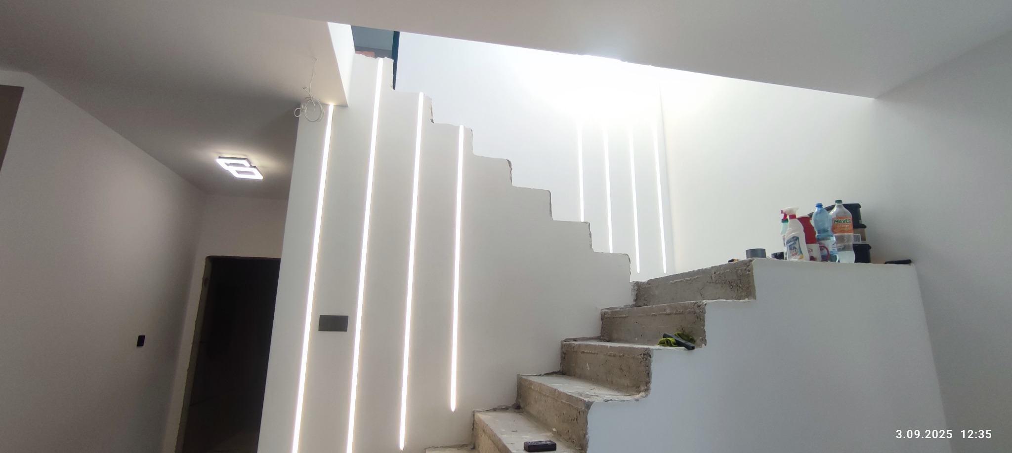 Nowoczesne schody z podświetleniem LED wzdłuż stopni, widoczne przewody. Świeże, białe ściany, minimalistyczny design. Częściowo wykończone, widoczne materiały budowlane.