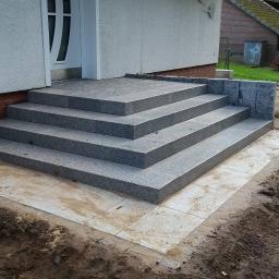 Truszkowski - Granitowe schody wejściowe z czterema stopniami prowadzące do domu, z wykończonym obrzeżem z jasnych płyt i częściowo przygotowanym terenem wokół.