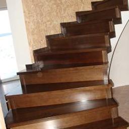 Usługi Stolarskie Elżbieta Świerszcz - Drewniane schody o ciemnobrązowym wybarwieniu, widok z dołu, z delikatnym wzorem na ścianie w tle.