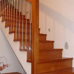 Usługi Stolarskie Elżbieta Świerszcz - Schody drewniane z metalowymi balustradami, widoczne z dołu, z koszem wiklinowym i fragmentem butów u podstawy.