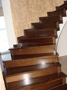 Drewniane schody o ciemnobrązowym wybarwieniu, widok z dołu, z delikatnym wzorem na ścianie w tle.