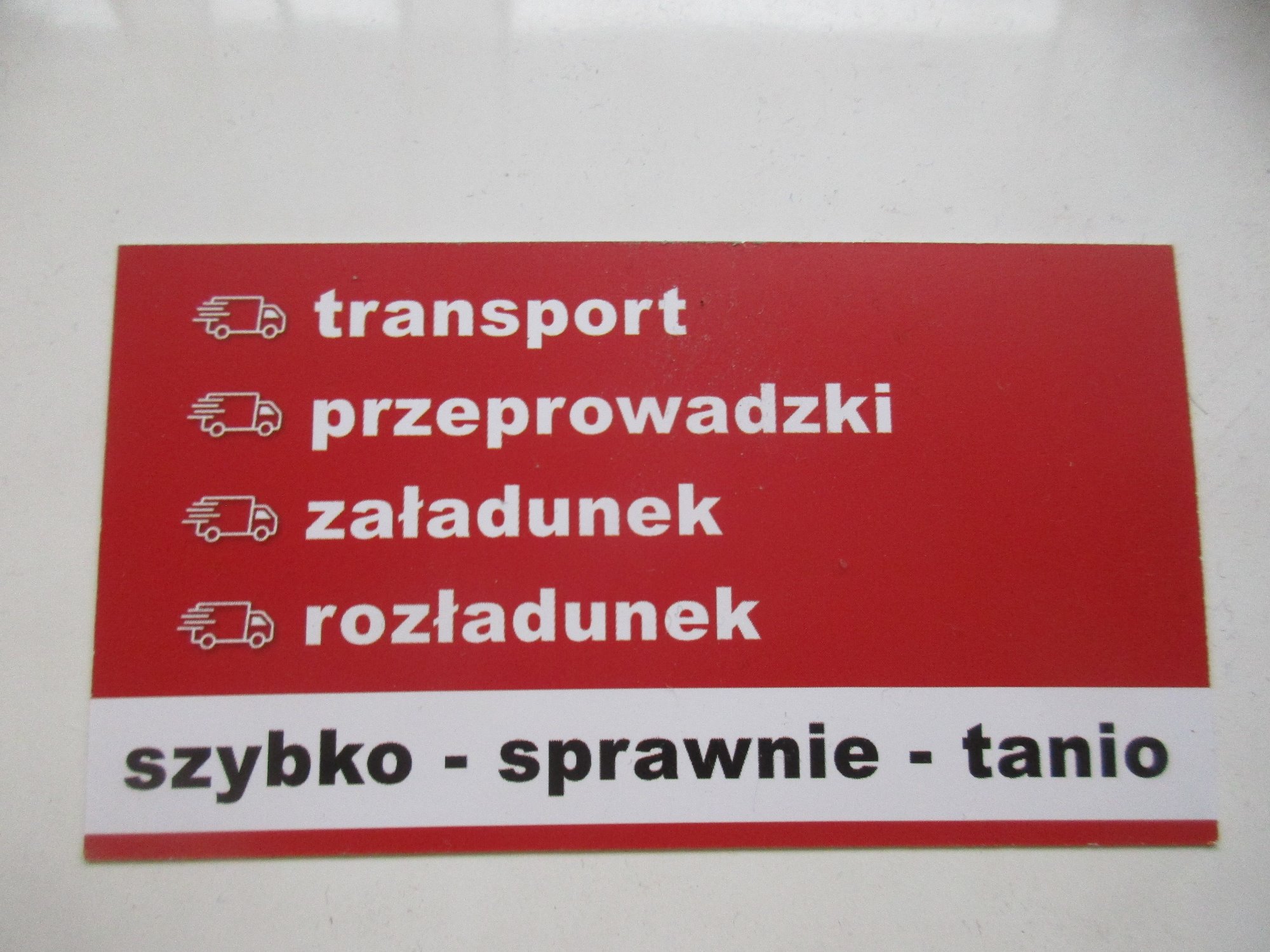 Czerwona wizytówka z białymi napisami: transport, przeprowadzki, załadunek, rozładunek, szybko - sprawnie - tanio, obok każdej usługi ikona ciężarówki.