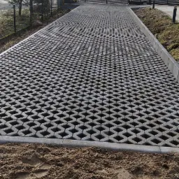 Ułożona nawierzchnia z ażurowych płyt betonowych prowadząca do bramy posesji w Szymbarku, z widocznymi śladami prac ziemnych i podsypką piaskową.