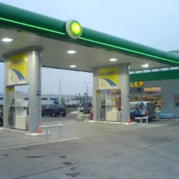 Stacja benzynowa w Szczecinku z charakterystycznym zielonym oświetleniem i szarymi kolumnami pod zadaszeniem, widoczny budynek sklepu z nazwą LEP i zaparkowany samochód osobowy w tle.