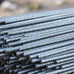 Stos żebrowanych pręt&oacute;w zbrojeniowych ułożonych r&oacute;wnolegle, widoczne ślady korozji na powierzchni.