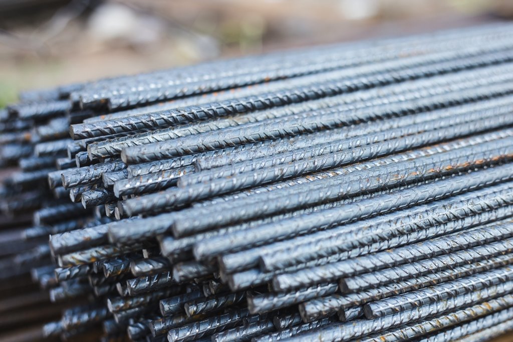 Stos żebrowanych prętów zbrojeniowych ułożonych równolegle, widoczne ślady korozji na powierzchni.