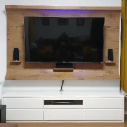 Ściana telewizyjna z drewnianą obudową i podświetleniem LED, biała szafka RTV z szufladami, głośniki na półkach, żółte zasłony po bokach.