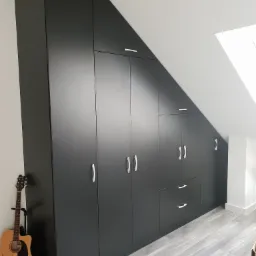 Czarna szafa wnękowa na poddaszu ze srebrnymi uchwytami, obok gitara akustyczna oparta o ścianę