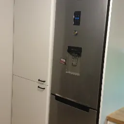 Biała zabudowa kuchenna ze srebrną lodówką Samsung w Zbychowie, czarne uchwyty, drewniana podłoga.