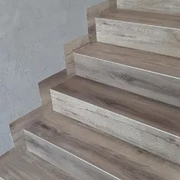 Wykończone schody z paneli imitujących drewno, widoczne szare ściany i fragment węża od odkurzacza.