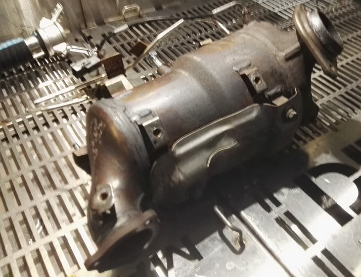 Używany katalizator samochodowy na metalowej kratownicy, widoczne ślady eksploatacji i spawania.