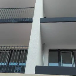 Widok z dołu na balkony z szarymi balustradami i okna w nowoczesnym budynku, jasna elewacja.