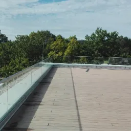 Wykończony taras na dachu w Słupsku z drewnianą podłogą i szklaną balustradą, widok na okoliczną zieleń.