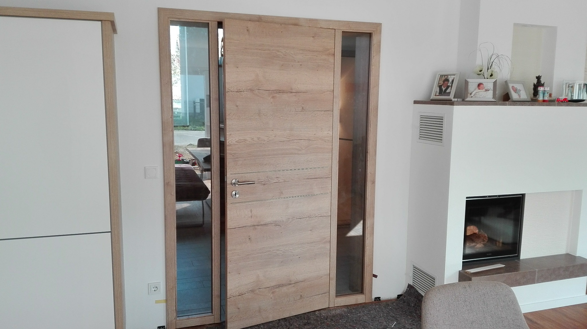 Drewniane drzwi przesuwne z elementami szkła, zamontowane w nowoczesnym wnętrzu z kominkiem, widoczne ślady montażu na podłodze.