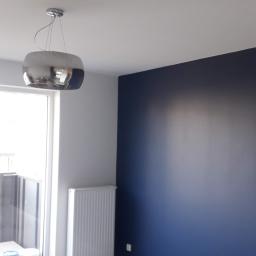 martom-lux - Pomalowane na granatowo wnętrze pokoju z grzejnikiem, lampą wiszącą i podłogą imitującą drewno, z parą czarnych butów na podłodze.