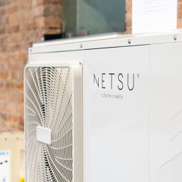 Instalacje Fotowoltaiczne i pompy ciepła GP-SYSTEMS - Biała pompa ciepła monoblok marki Netsu z widocznym wentylatorem i napisem 'czyste ciepło' na tle ceglanej ściany i ulotki informacyjnej.