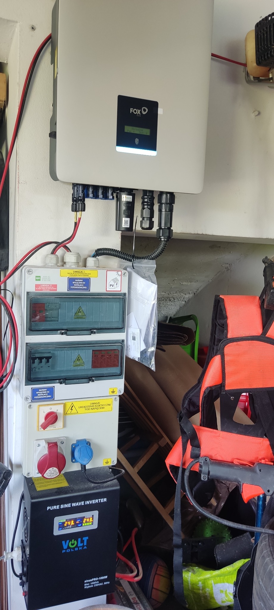 Rozdzielnica elektryczna z zabezpieczeniami, inwerter Volt Polska sinusPRO-1000W, oraz inwerter FOX ESS zamontowane na ścianie, z widocznymi przewodami i elementami instalacji fotowoltaicznej.