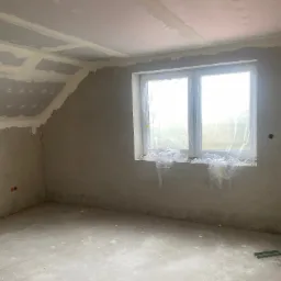 Pokój po szpachlowaniu w Nowej Soli, przygotowany do malowania. Widoczne zabezpieczone okno folią malarską, ściany przygotowane pod gładzie i sufit z płyt gipsowych.