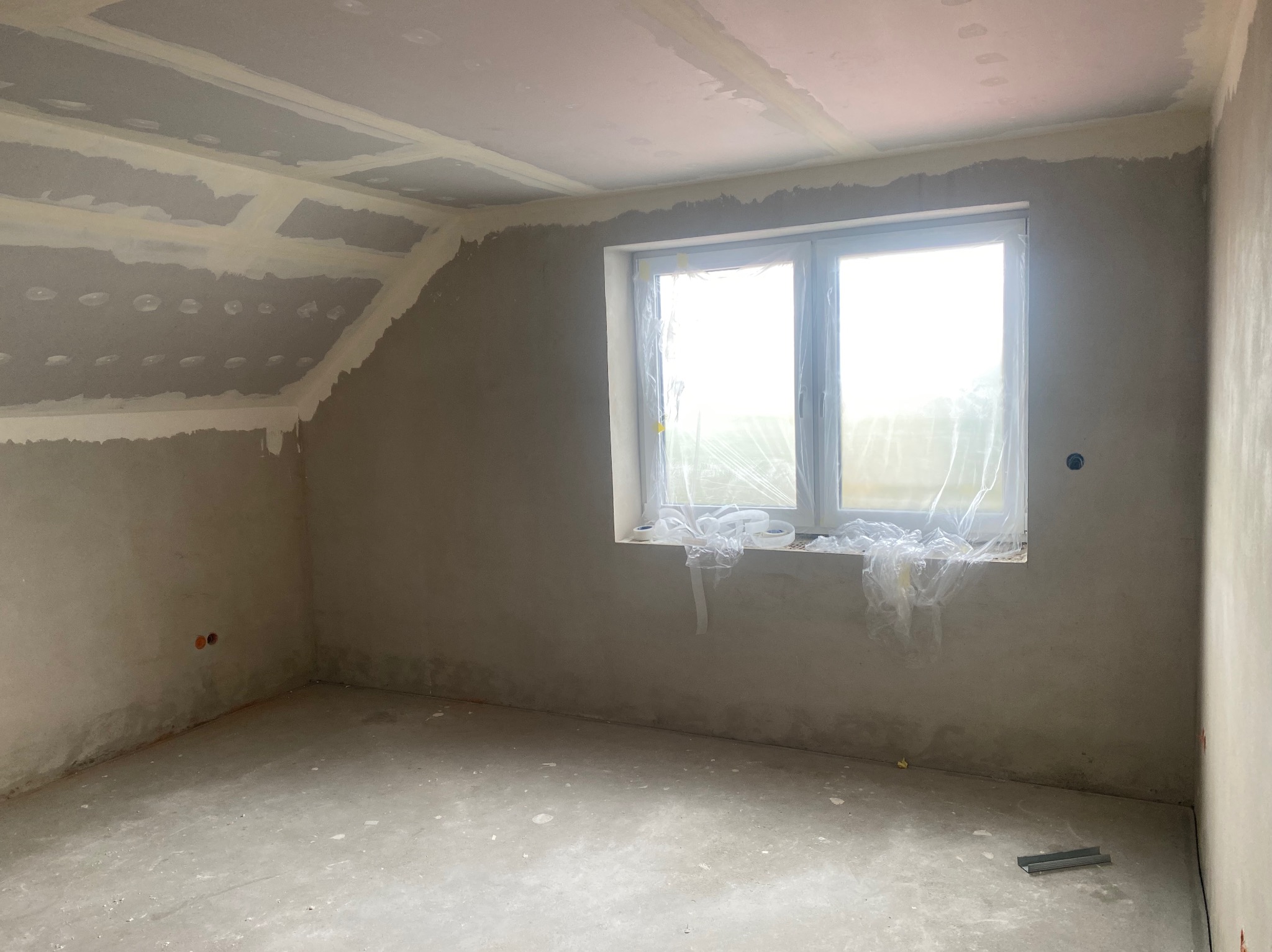 Pokój po szpachlowaniu w Nowej Soli, przygotowany do malowania. Widoczne zabezpieczone okno folią malarską, ściany przygotowane pod gładzie i sufit z płyt gipsowych.