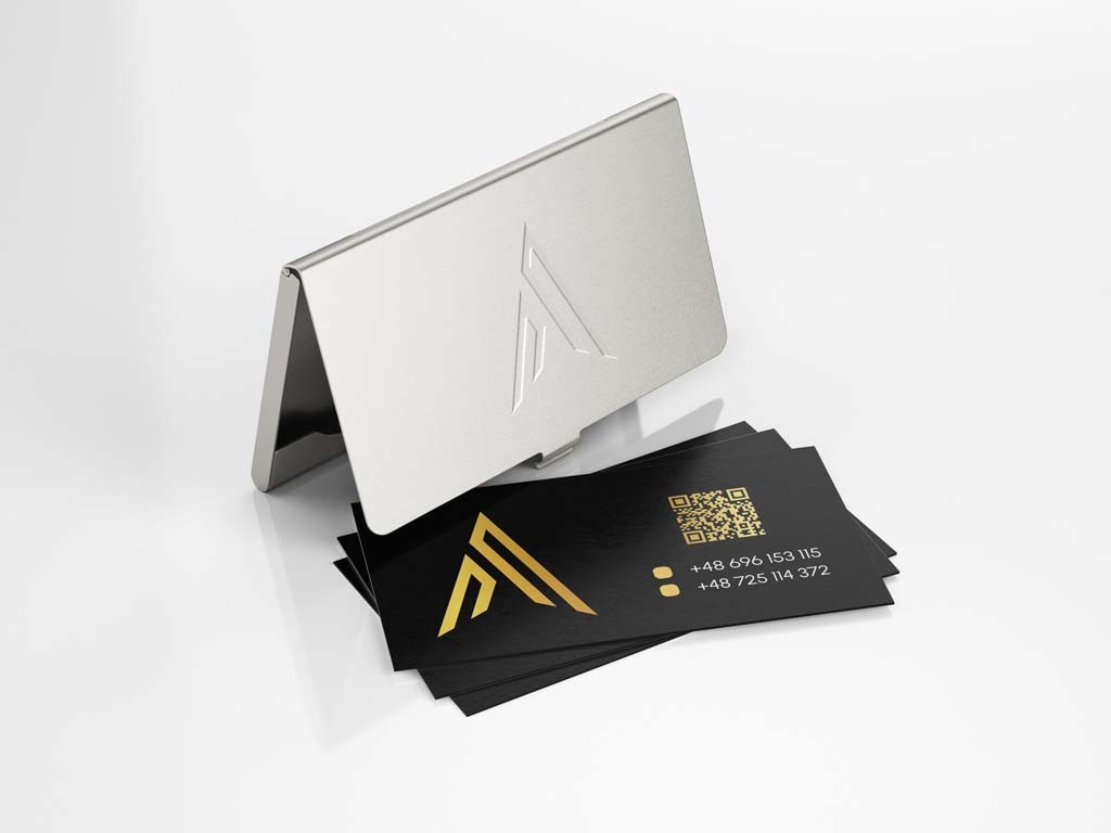Stylowe czarne karty z błyszczącym złotym logo i kodem QR, ułożone obok otwartego metalowego wizytownika z wytłoczonym logo na białym tle.