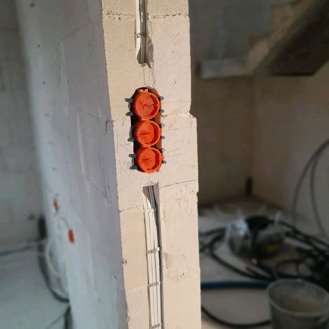 Pomarańczowe puszki elektryczne zamontowane w surowej ścianie z betonu komórkowego. Widoczne kable w bruzdach. Etap prac przed tynkowaniem.