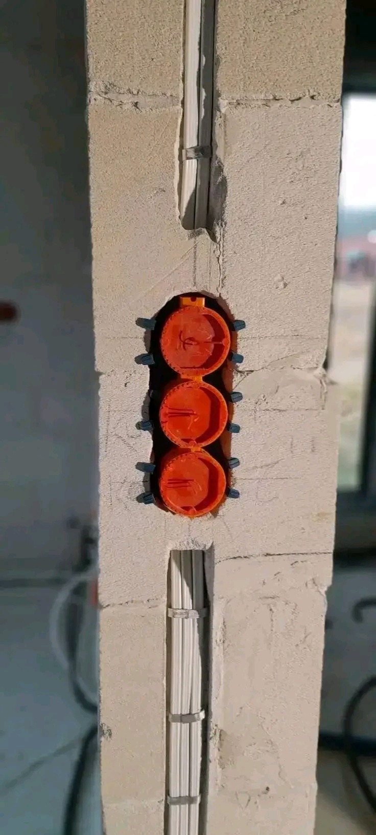 Wykute bruzdy w ścianie z zamontowanymi puszkami elektrycznymi i peszlami z kablami. Widoczne mocowania. Ściana z betonu komórkowego.