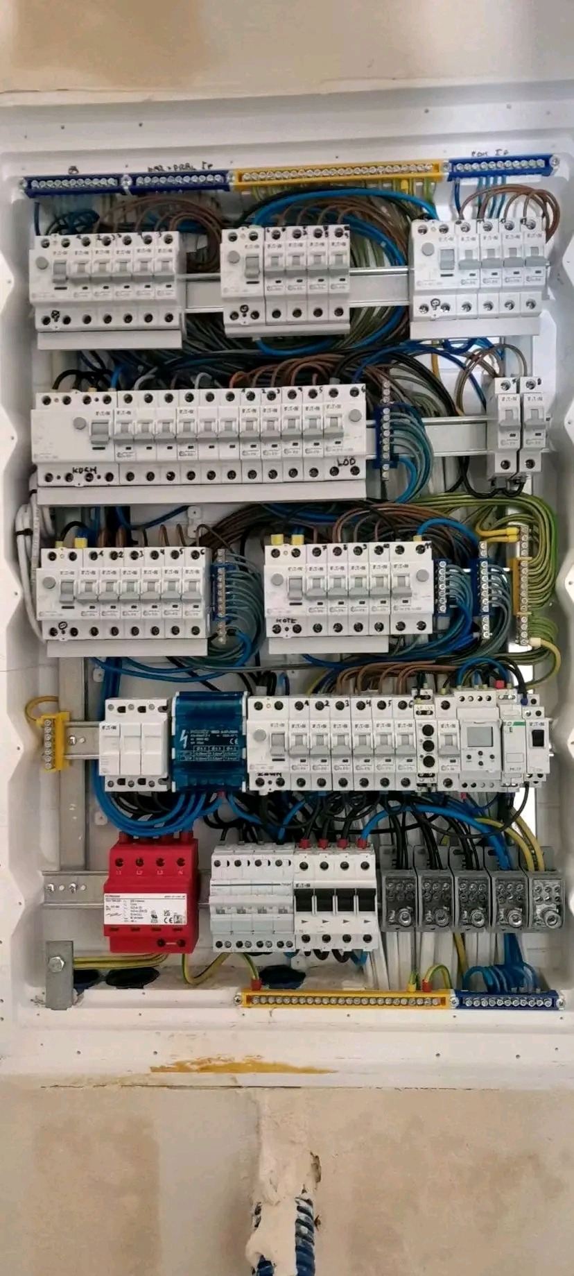 Rozdzielnica elektryczna z bezpiecznikami, przewodami i elementami zabezpieczającymi, zamontowana w białej obudowie. Widoczne kable i listwy zaciskowe.