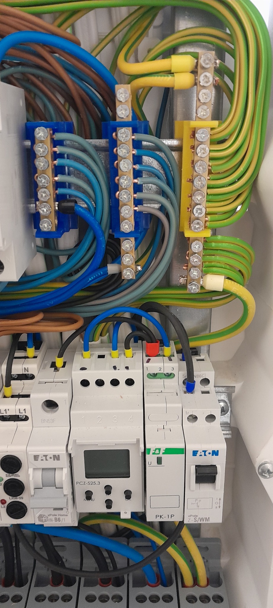 Rozdzielnica elektryczna z bezpiecznikami Eaton, przewodami w różnych kolorach i listwami zaciskowymi. Widok z bliska na podłączenia w skrzynce.
